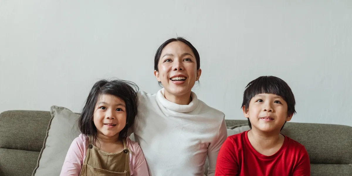 A mother and two young children sitting on a sofa, all smiling up at a screen out of frame
